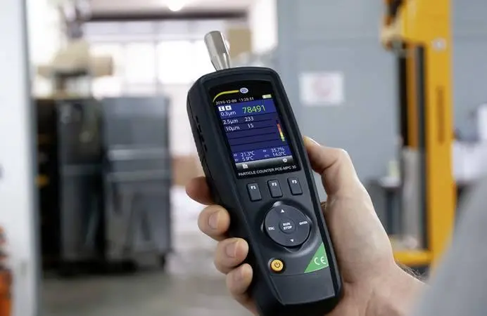 Technician using a handheld particle counter to perform total particulate testing for indoor air quality monitoring.